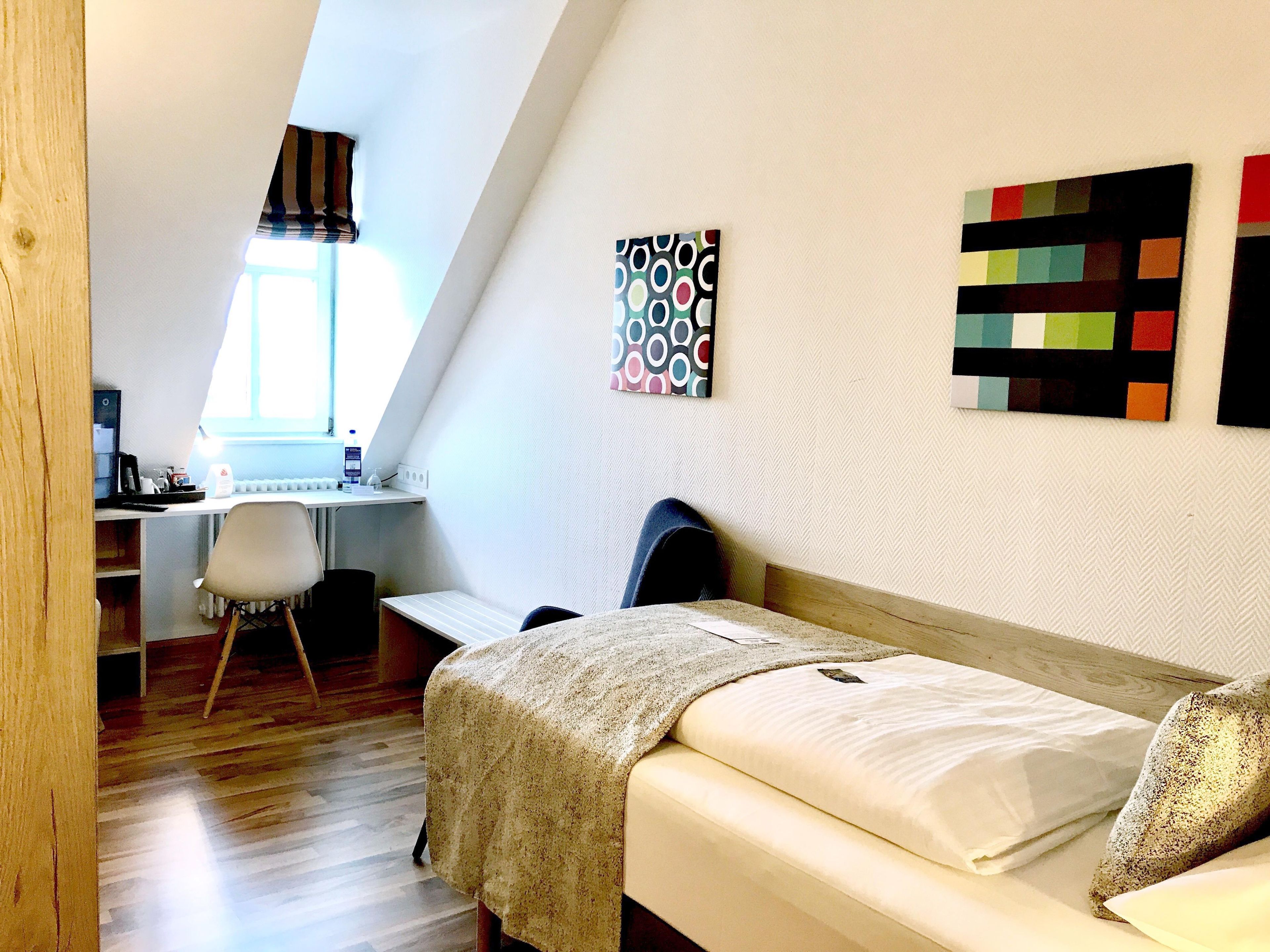 A bedroom with a bed, a desk, and a chair. There is a window providing natural light.