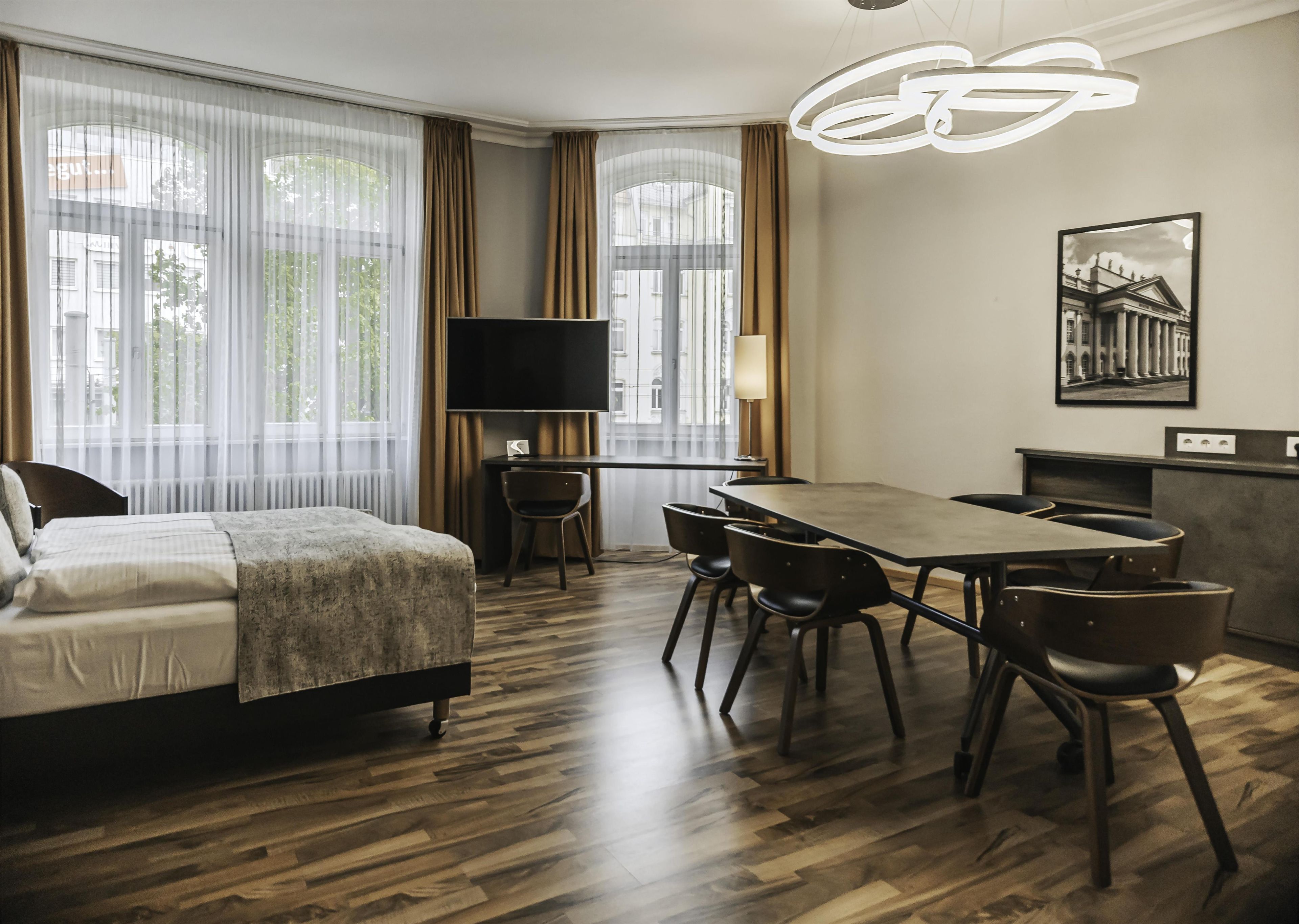 A hotel room with a bed, a desk, a chair, a television, and a dining table with chairs.