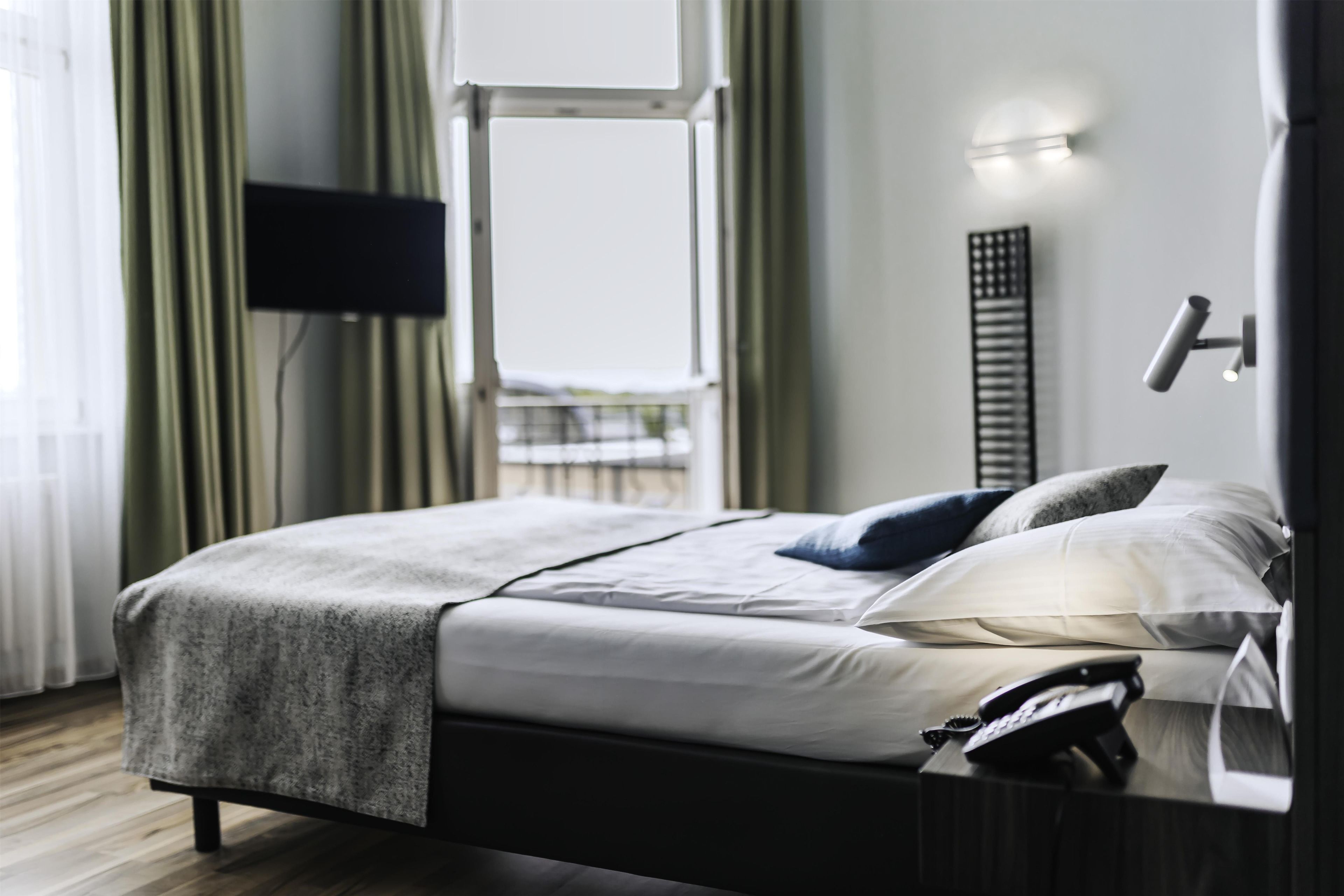 Una habitación de hotel moderna con una cama, un televisor de pantalla plana, una mesita de noche y una ventana con cortinas.