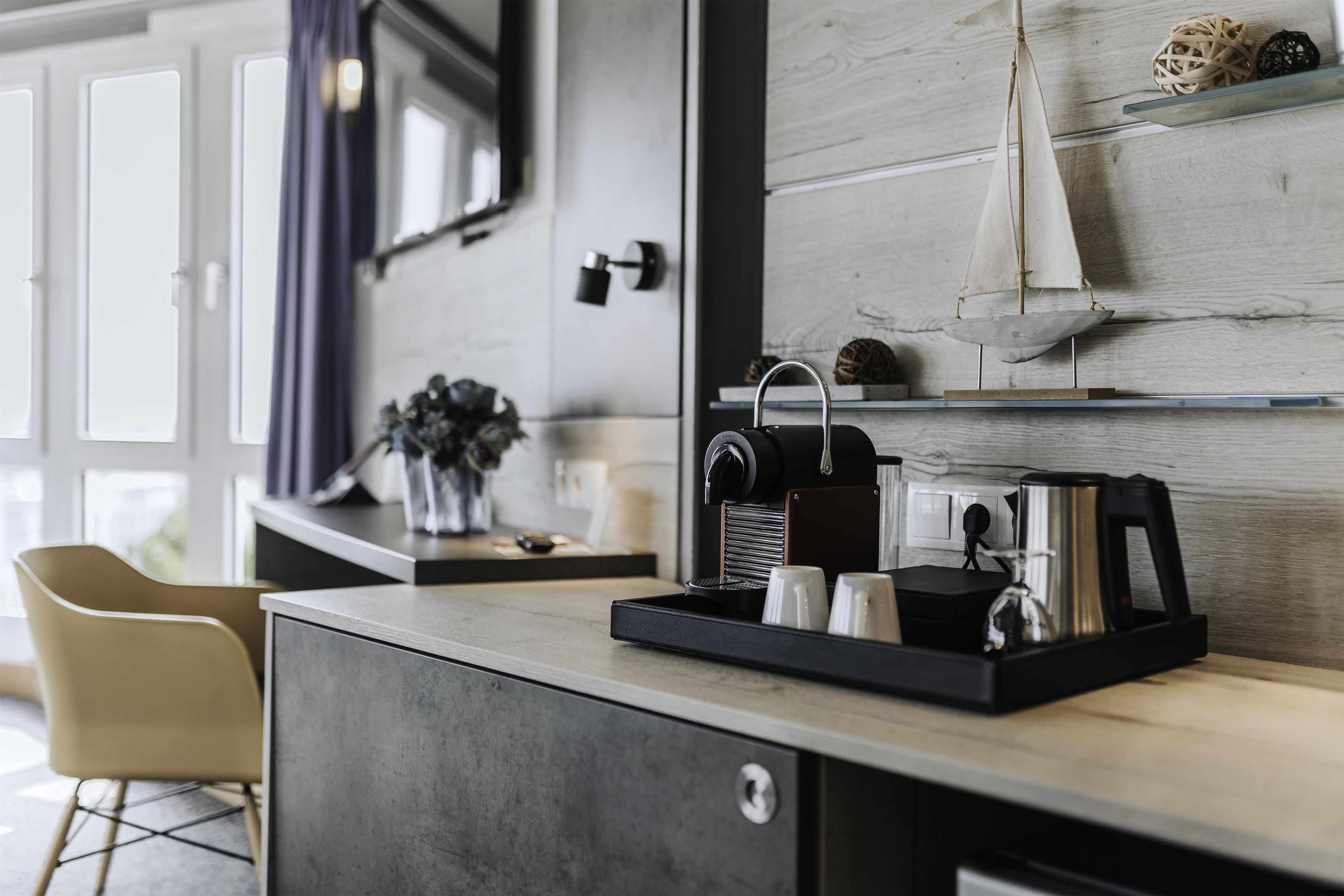Una kitchenette moderna con cafetera, tetera y un pequeño estante con adornos.