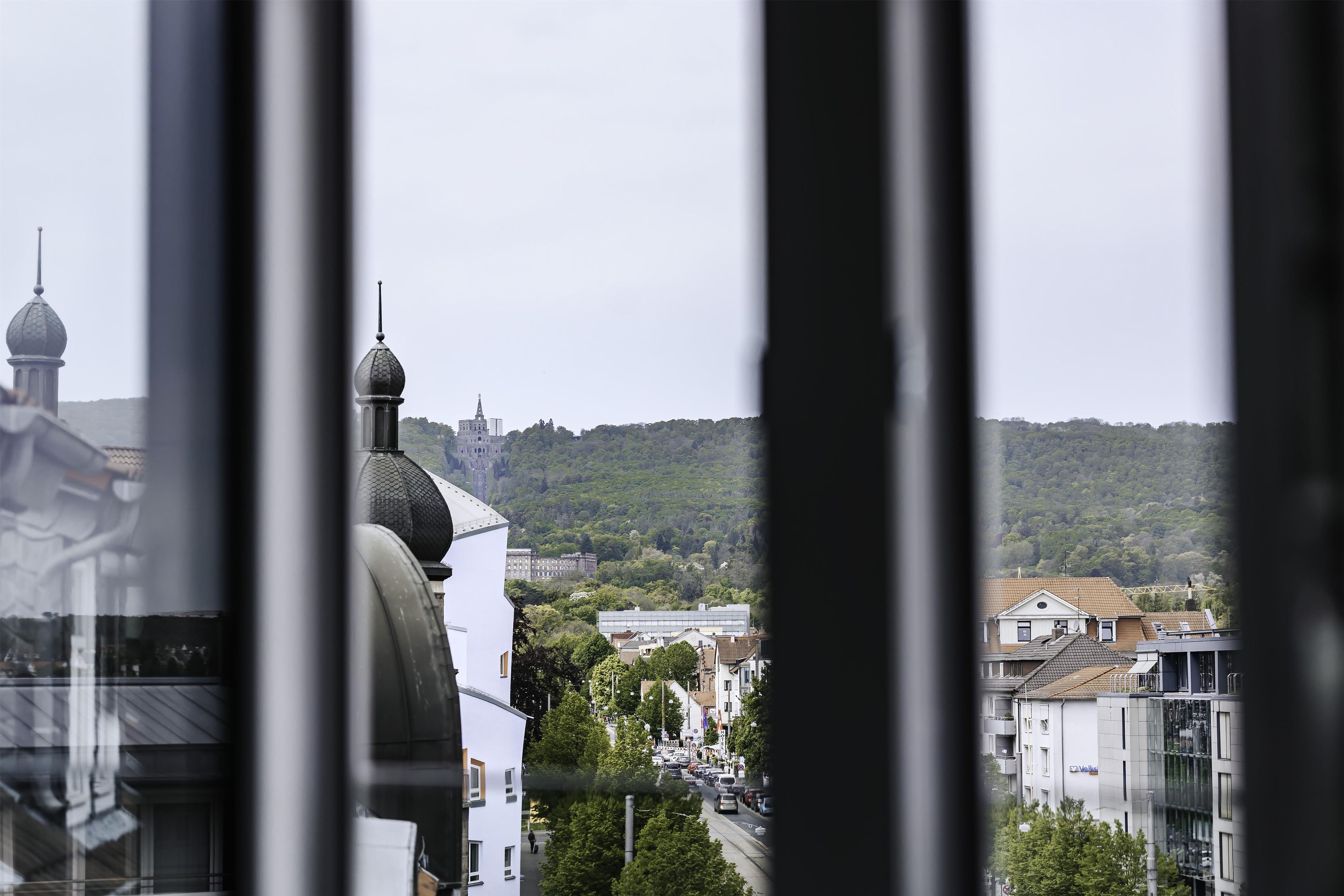 Vista de un paisaje urbano con una cúpula de iglesia destacada y una colina cubierta de vegetación densa al fondo.