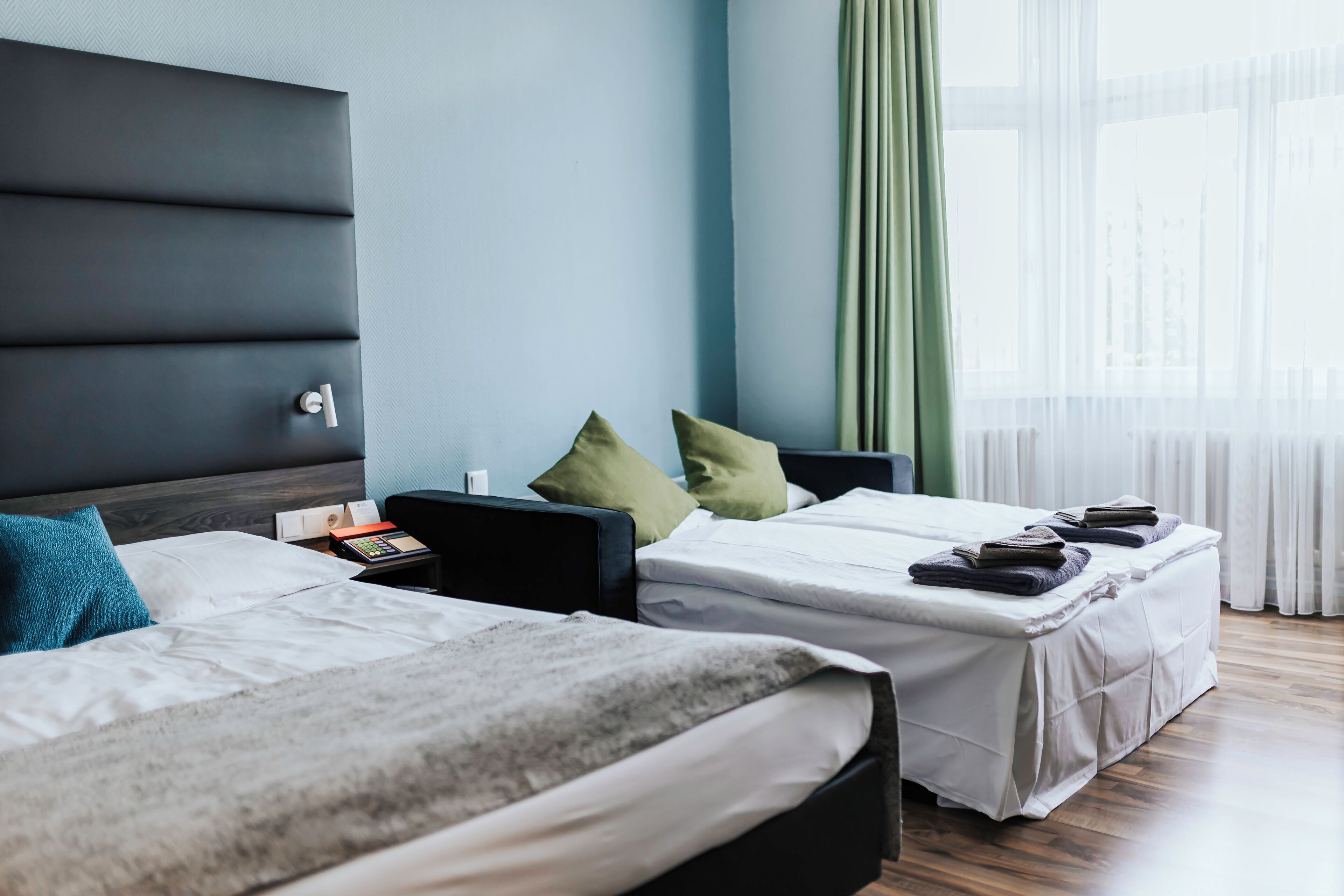 Habitación de hotel con dos camas, una mesita de noche, una lámpara y una ventana con cortinas.