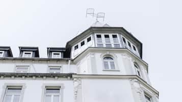 A corner of a building with a white facade, multiple windows, and a distinct architectural style with decorative moldings.