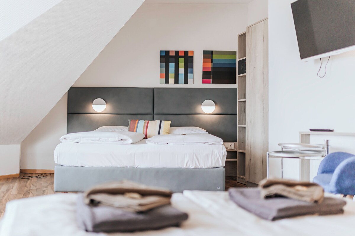 A modern bedroom with a bed, bedside lamps, a TV, and a bookshelf.
