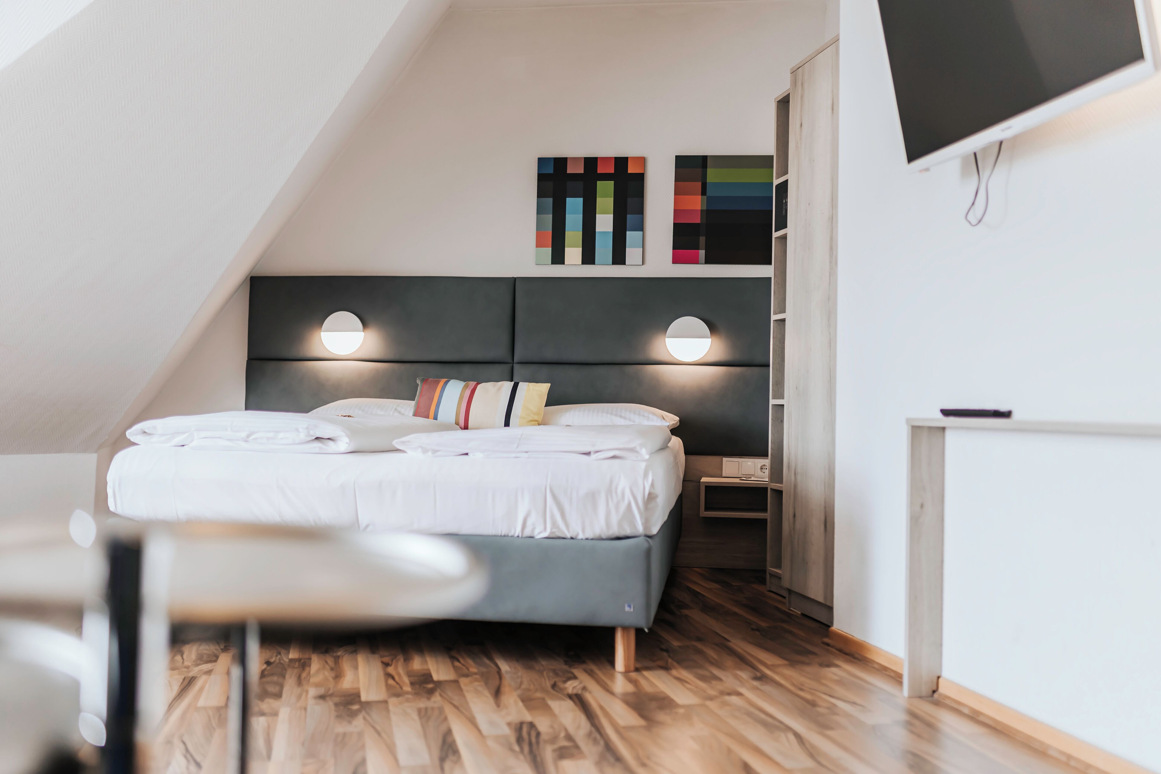Une chambre moderne avec un lit, des lampes de chevet, un téléviseur et un plancher en bois.