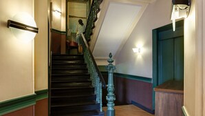 A staircase with a wooden handrail and a green balustrade leading to an upper floor.