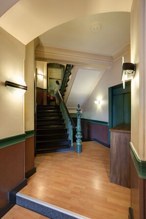 A staircase with a wooden handrail and a green balustrade leading to an upper floor.