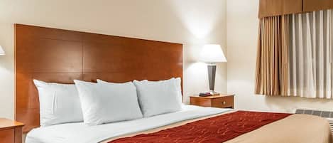 Habitación de hotel con una cama grande, cabecera de madera, mesita de noche con lámpara y ventana con cortinas.
