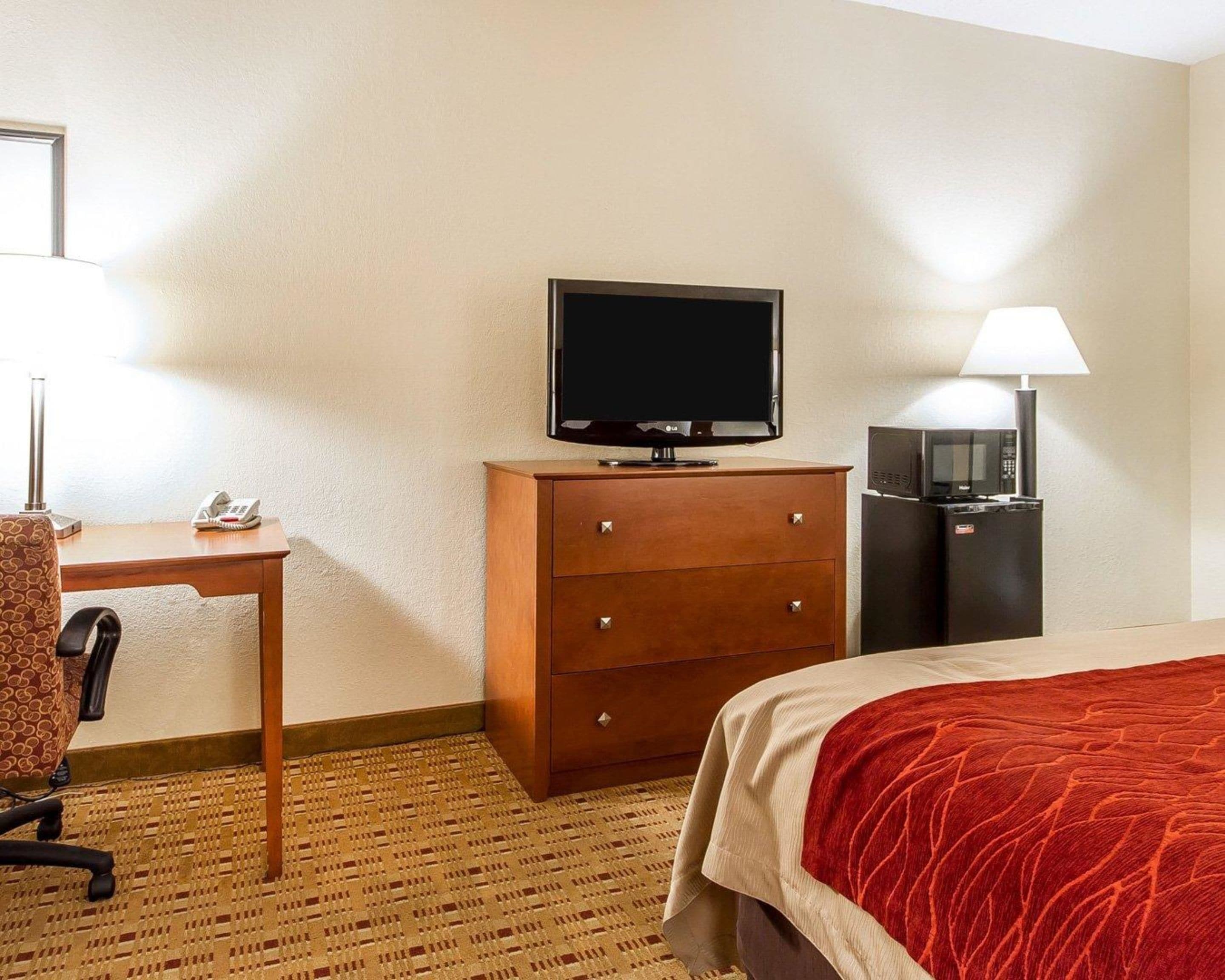 A hotel room with a bed, a desk with a telephone, a television, a minibar, and a lamp.