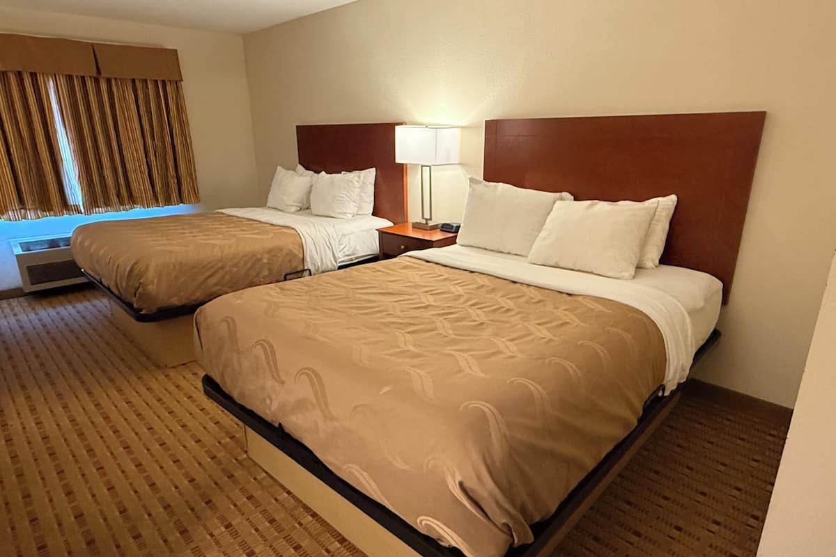 A hotel room with two beds, a nightstand with a lamp, and a window with curtains.