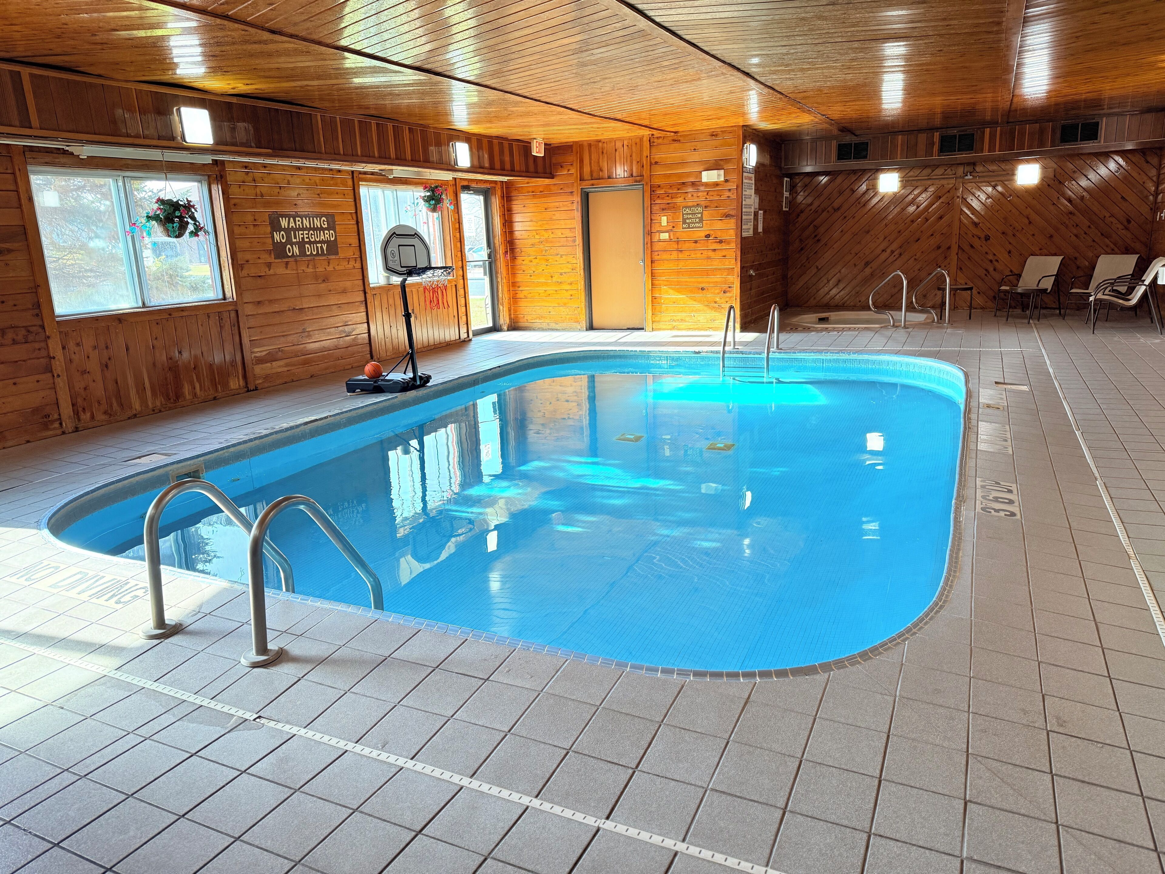 An indoor swimming pool with clear water, wooden walls, and tiled flooring.