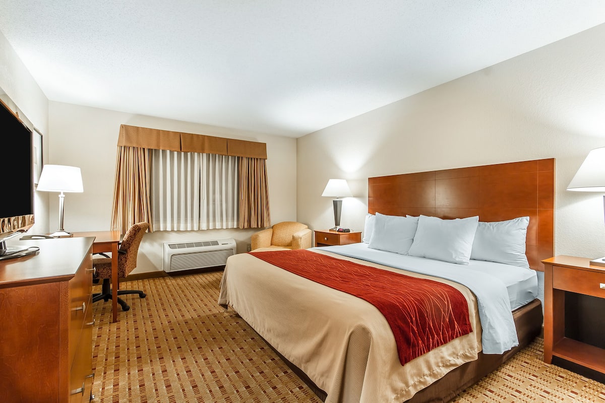 A hotel room with a large bed, a desk, a chair, a TV, and a window with curtains.