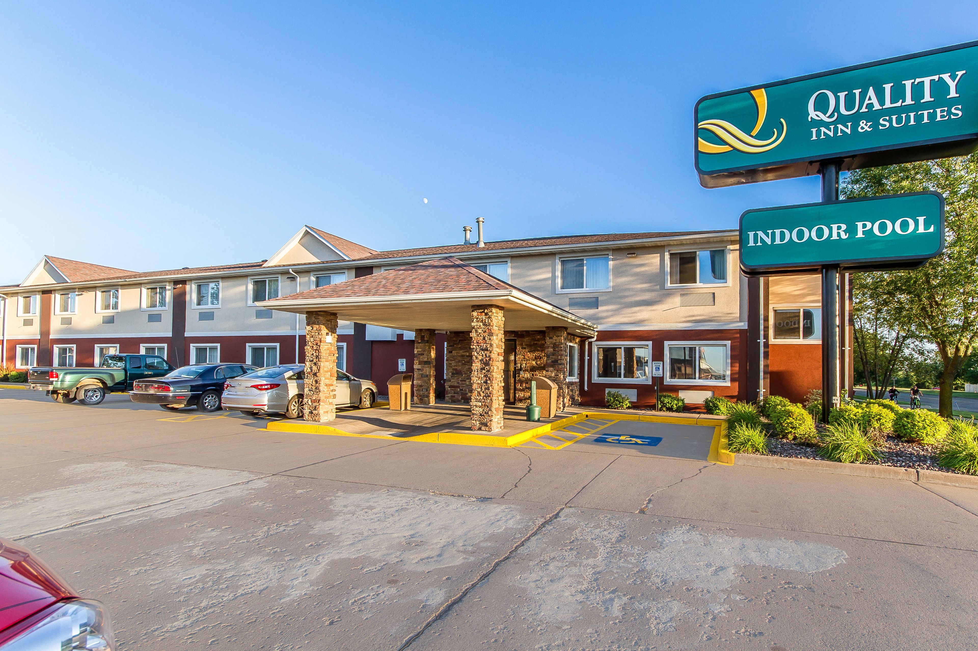 A hotel with an indoor pool, a covered entrance, and a parking lot with several cars.