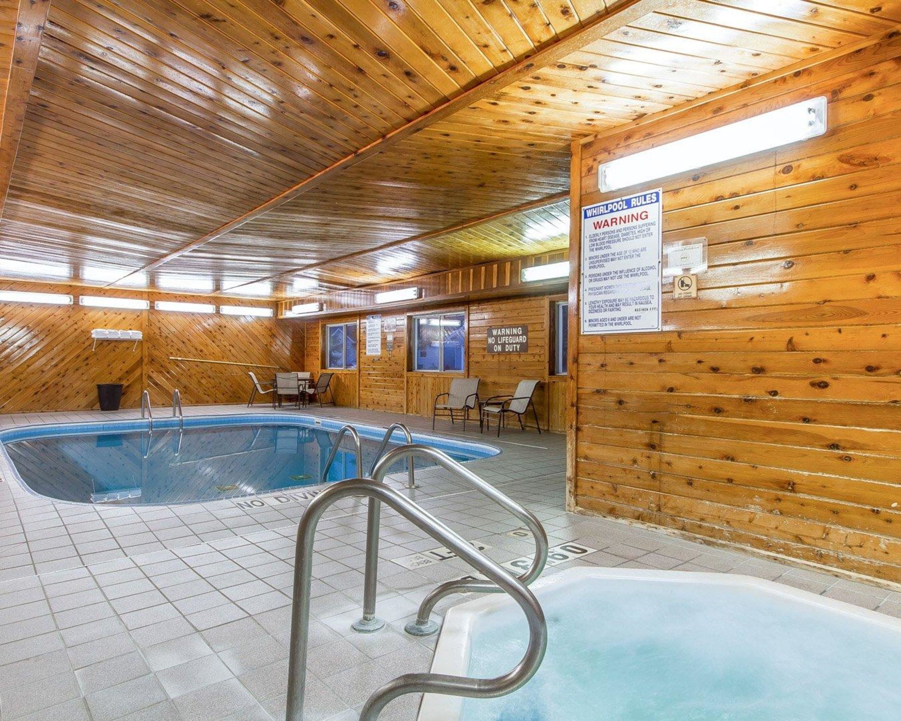 An indoor swimming pool with wooden walls and a tiled floor. There are signs indicating whirlpool rules and a warning that no lifeguard is on duty.