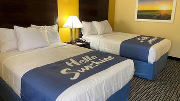 A hotel room with two beds, a nightstand with a lamp, and a painting of a sunset on the wall.