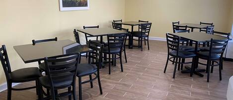 A dining area with multiple tables and chairs, a flat-screen TV mounted on the wall, and a framed picture of a sunset.