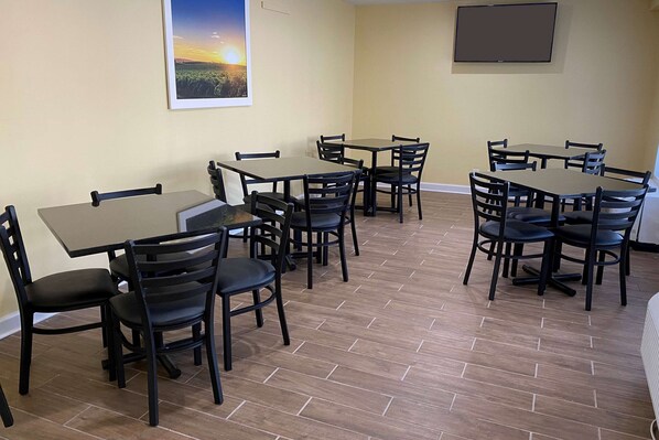 A dining area with multiple tables and chairs, a flat-screen TV mounted on the wall, and a framed picture of a sunset. - Days Inn by Wyndham Atlanta/Southlake/Morrow (Morrow)