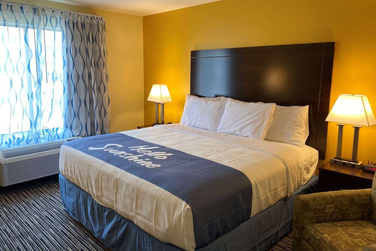 A hotel room with a large bed, two bedside lamps, a window with curtains, and a wall heater.