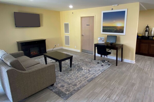 A living room with a sofa, coffee table, TV, fireplace, and a desk with a computer. - Days Inn by Wyndham Atlanta/Southlake/Morrow (Morrow)