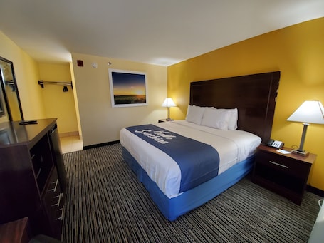 A hotel room with a large bed, two bedside lamps, a nightstand, a desk with a telephone, a mirror, and a picture of a sunset on the wall.