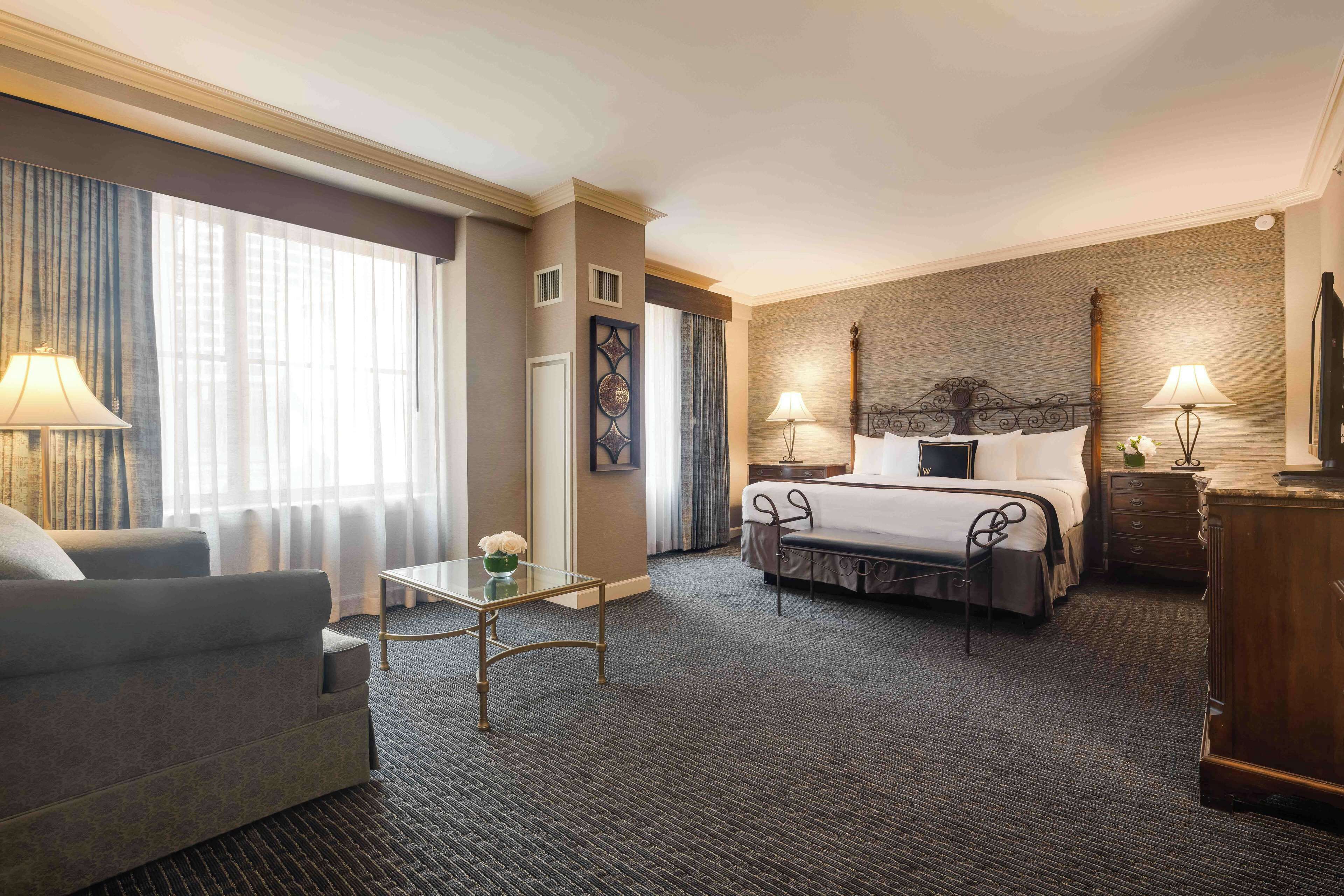 A hotel room with a bed, a sofa, a small table, and a lamp.