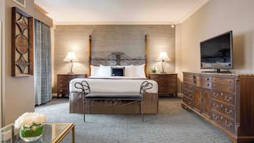 Une chambre d’hôtel avec un grand lit, deux tables de chevet avec des lampes, une télévision, une commode en bois et une petite table sur laquelle est posé un vase de fleurs.
