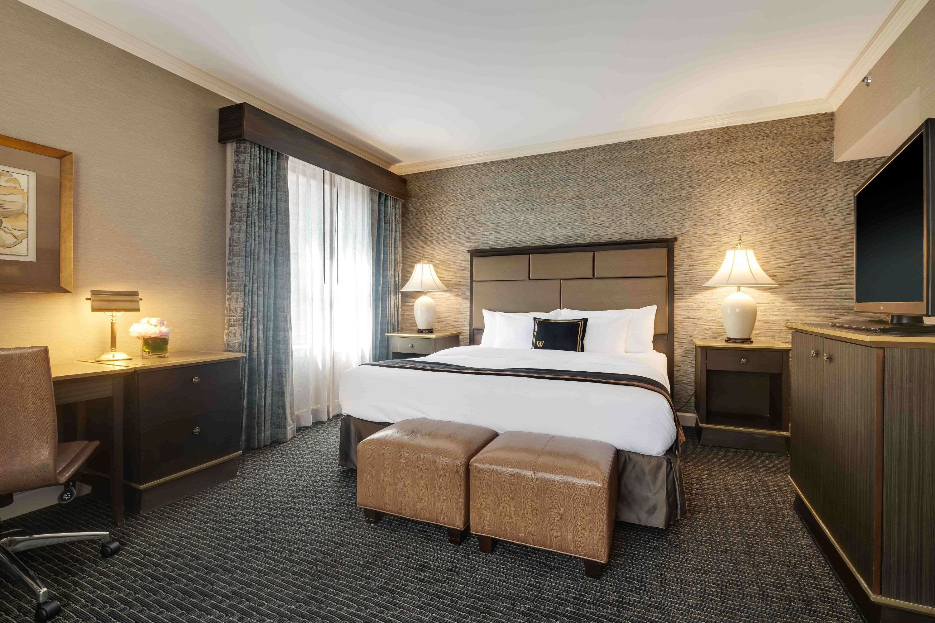 A hotel room with a large bed, two bedside tables with lamps, a desk with a chair, and a TV.