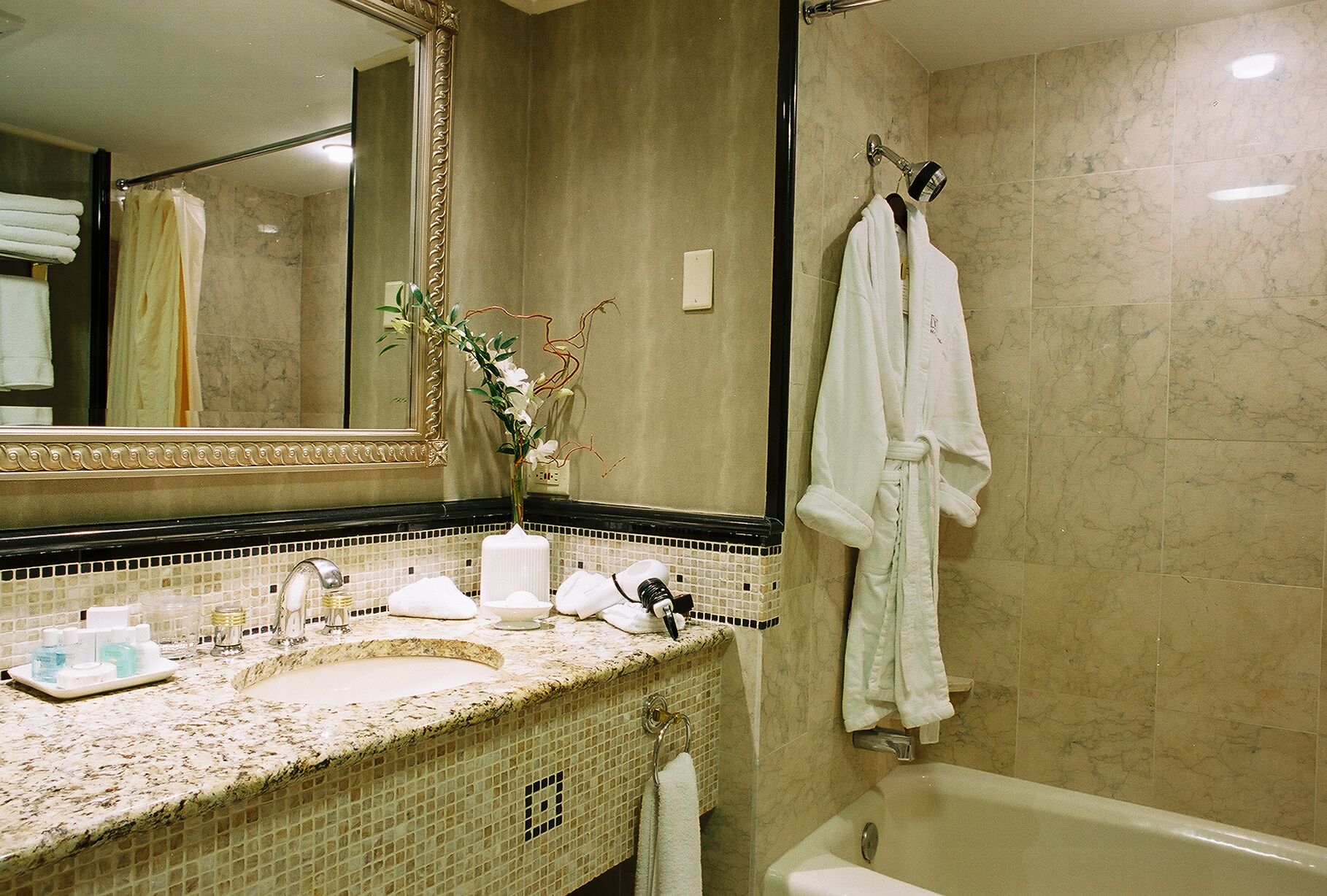 Un bagno con lavabo in marmo, uno specchio grande, una vasca da bagno e un porta asciugamani.