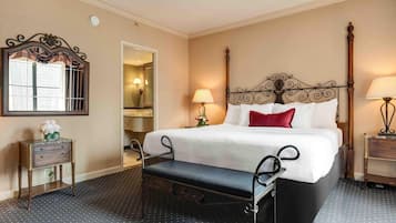 A hotel room with a large bed, a bench, a bedside table, a mirror, and a lamp.