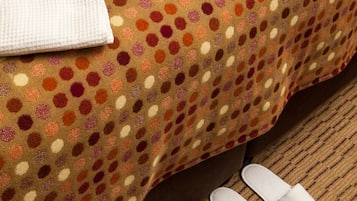 Un lit recouvert d’une couvre-lit à pois, deux serviettes blanches ornées de monogrammes et une paire de chaussons blancs posés sur le sol.