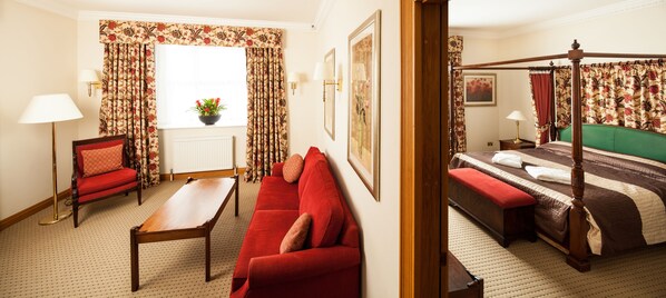 A hotel room with a four-poster bed, a red sofa, a wooden coffee table, and a potted plant by the window.