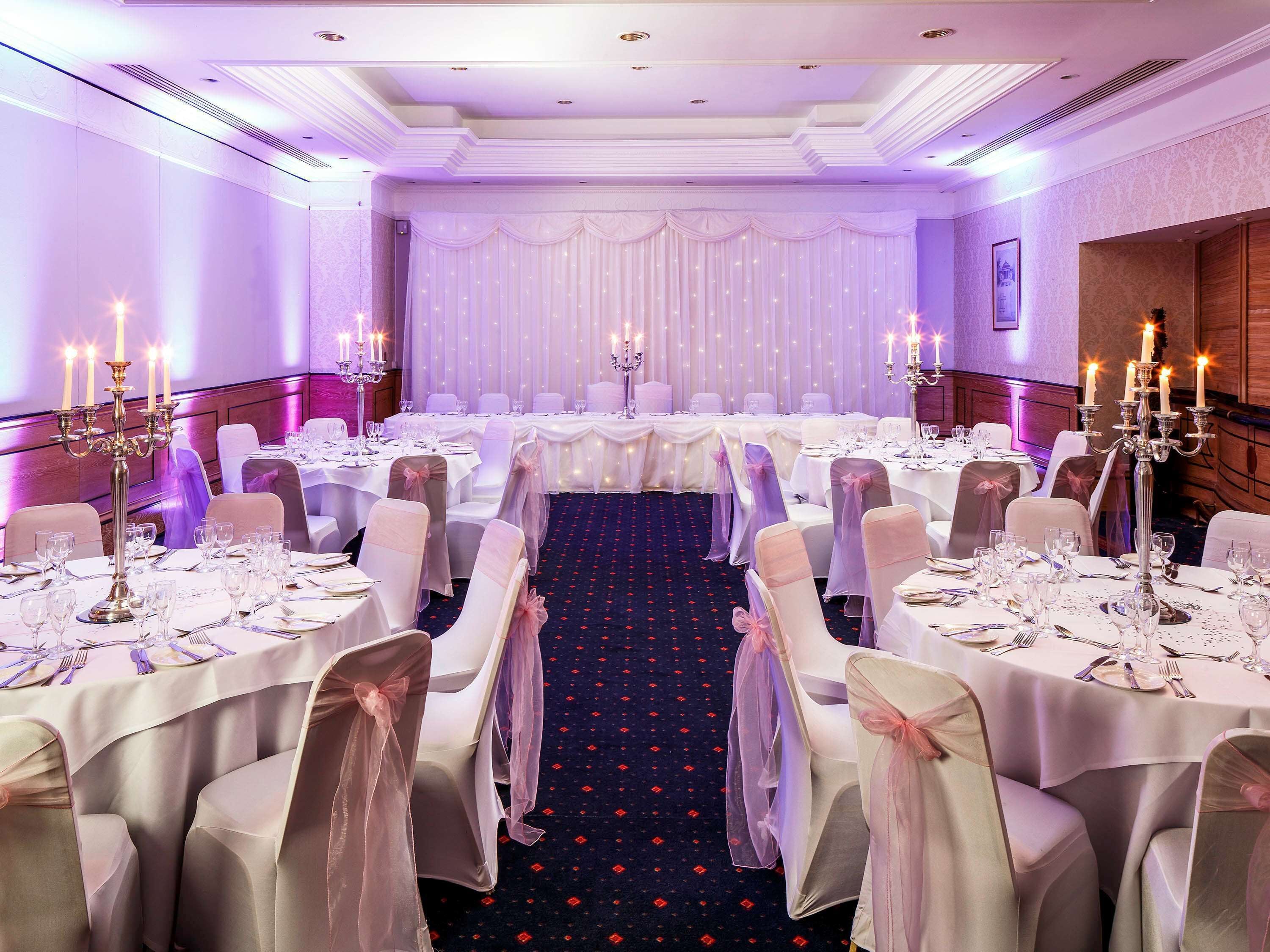 A banquet hall with round tables, white tablecloths, and chairs with pink sashes.