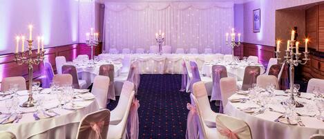 A banquet hall with round tables, white tablecloths, and chairs with pink sashes.