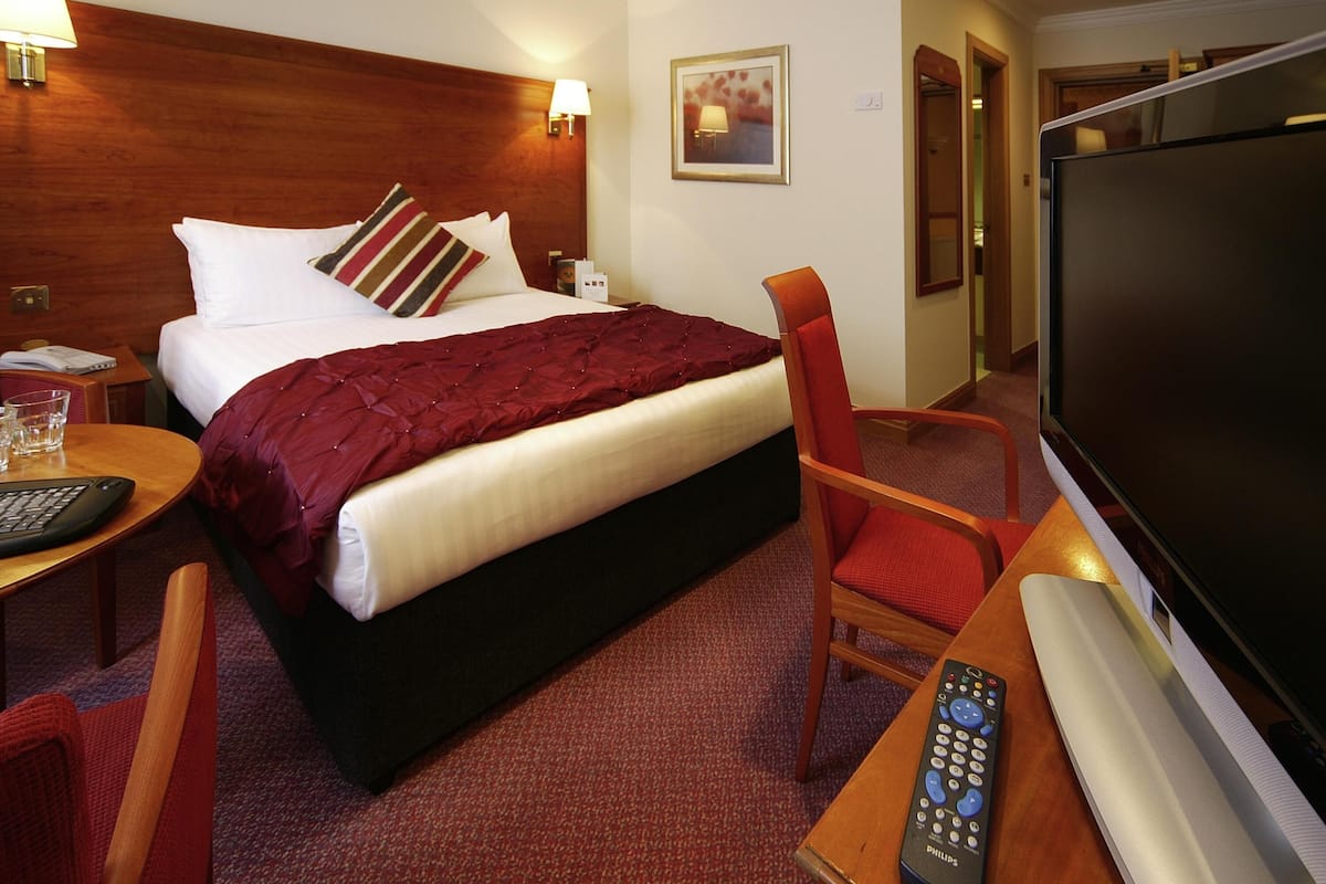 A hotel room with a bed, a desk with a computer, a TV, and a chair.