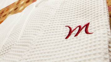 A neatly made bed with a white pillow featuring a red 'M' embroidery, a black pillow, and a polka-dotted pillow.