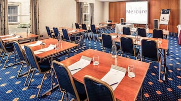 Un salón de conferencias con varias mesas y sillas, una pantalla de proyector mostrando 'Mercure', y una pizarra para presentaciones.