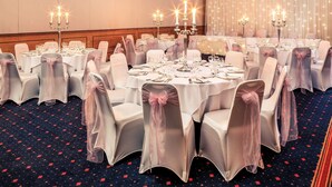 Un salón de banquetes con mesas redondas, manteles blancos y sillas con fundas de gasa.
