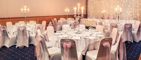 Un salón de banquetes con mesas redondas, manteles blancos y sillas con fundas de gasa.