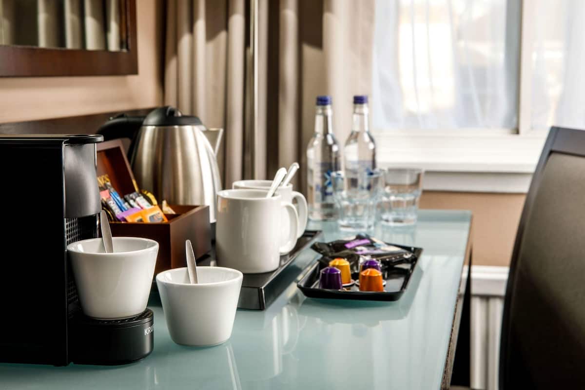 A hotel room with a kitchenette, including a coffee maker, cups, a tray with condiments, and a lamp.