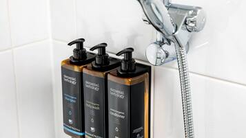 Tres botellas de champú, gel de baño y acondicionador de Elemental Herbology montadas en una pared cerca de una ducha.