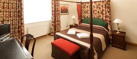 A four-poster bed with a green headboard, a wooden desk with a computer, and two bedside tables with lamps.