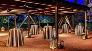 An outdoor event space with multiple round tables covered with beige tablecloths, illuminated by lanterns and pendant lights. - DoubleTree by Hilton Hotel Boston - Westborough (Westborough)