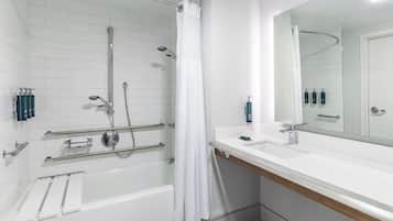 A modern bathroom with a white bathtub, a shower with a curved glass door, and a large mirror above the sink.