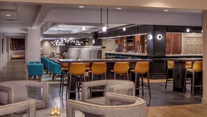 A modern hotel lobby with a bar area, seating arrangements, and a kitchen visible in the background. - DoubleTree by Hilton Hotel Boston - Westborough (Westborough)