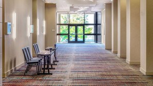A hotel corridor with a patterned carpet, rows of chairs, and a large window with a view of trees. - DoubleTree by Hilton Hotel Boston - Westborough (Westborough)