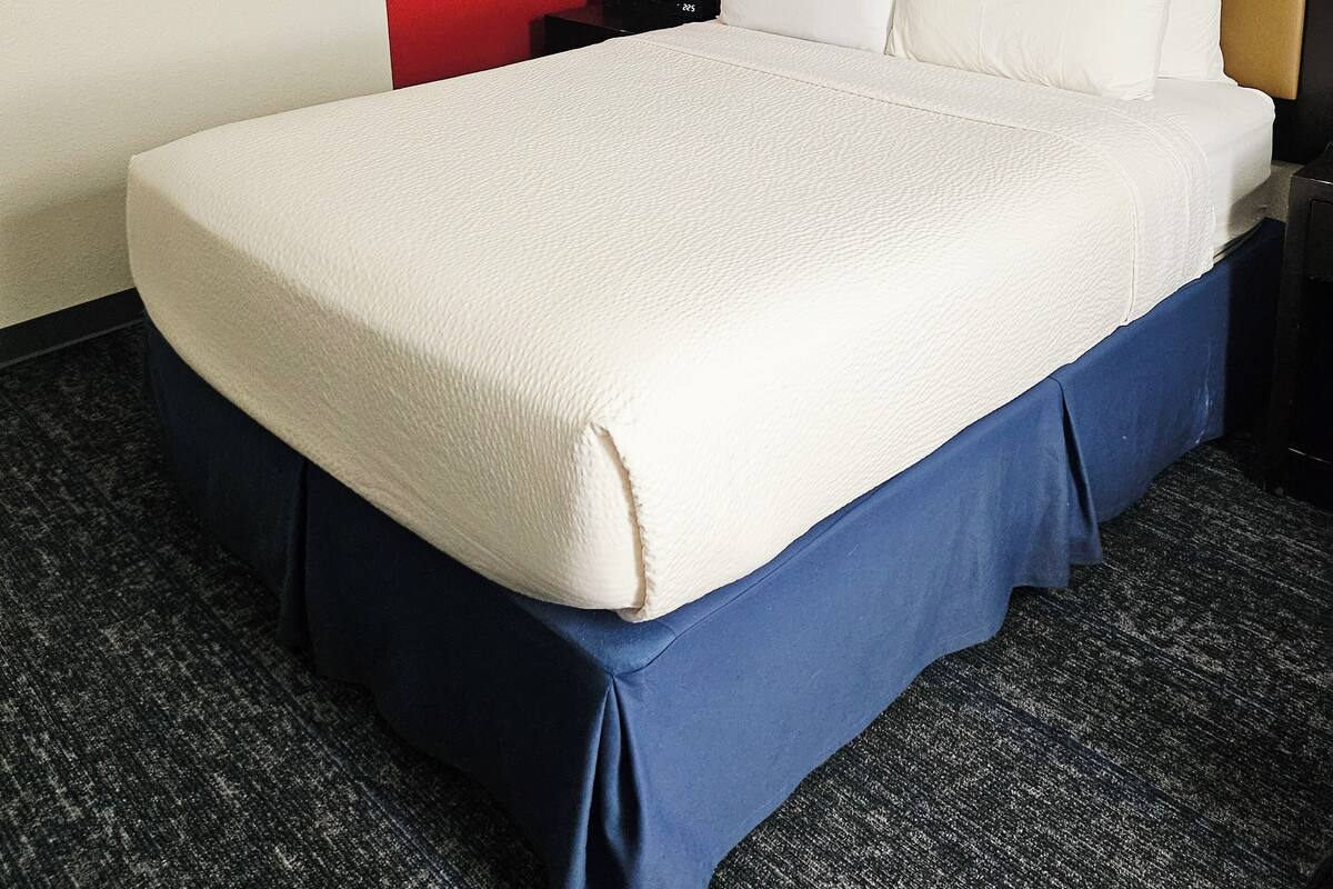 A hotel room with a large bed, a nightstand with a lamp, and a framed world map on the wall.