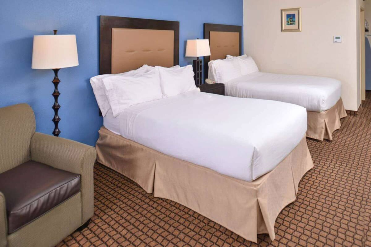 A hotel room with two beds, a chair, and a lamp.