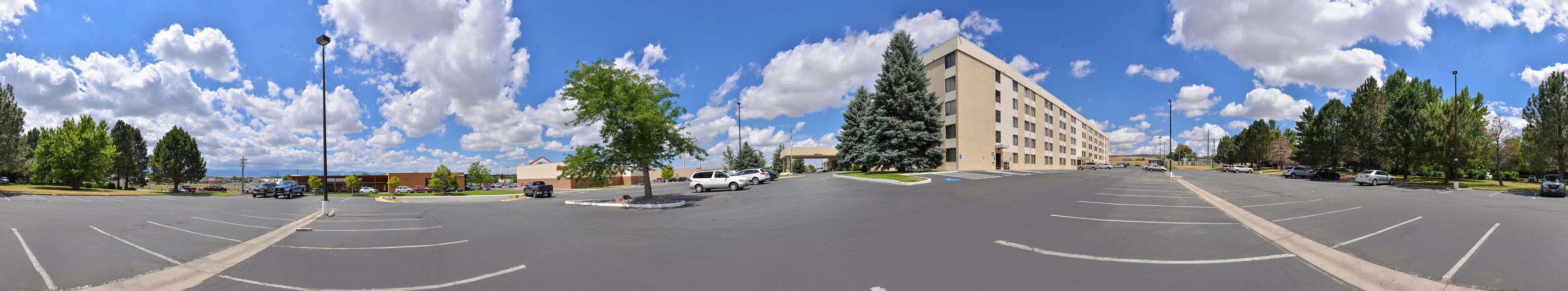 A parking lot with multiple cars, a large building with a flat roof, and several trees.