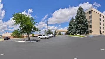 A parking lot with multiple cars, a large building with a flat roof, and several trees.