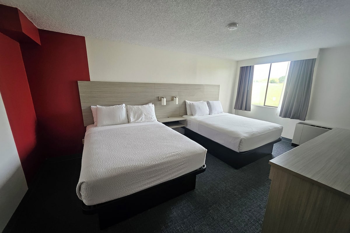 A hotel room with two beds, a desk, and a window with curtains.